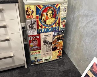 May include: A compact refrigerator covered in a collage of vintage-style beer and pub-themed advertisements. The front features various illustrations, including a portrait of a queen, text reading Campaign for Real Ales, Brewco, and Beer, and colorful graphics.