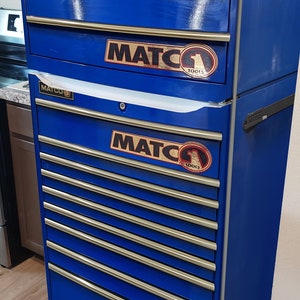 May include: A blue metal toolbox with multiple drawers. The toolbox has a silver handle and is labeled "MATCO TOOLS" on the front.