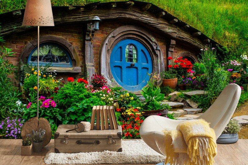 Pode incluir: Uma casa de hobbit de sonho com uma porta redonda azul, rodeada de vegeta&ccedil;&atilde;o exuberante e flores coloridas. Uma cadeira branca com um cobertor amarelo fica em primeiro plano.