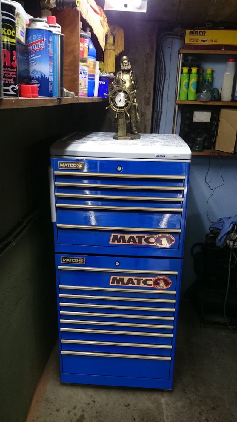May include: A blue metal toolbox with multiple drawers. The toolbox has the word "MATCO" printed on the front of each drawer. The toolbox is sitting on a concrete floor.