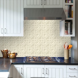 Puede incluir: Una cocina blanca con armarios blancos y una encimera negra. El salpicadero es de azulejos crema con un patrón geométrico. Una campana extractora de acero inoxidable está sobre la estufa.