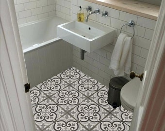 May include: A bathroom with white subway tile walls, a white bathtub, and a white sink. The floor features patterned tiles in shades of gray and white. A window and mirror are visible, along with a towel rack and a small trash can.