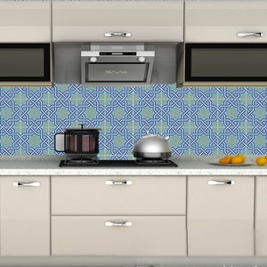 Op de afbeelding: Een keukenachterwand met een geometrisch patroon in blauw en groen. De achterwand is gemaakt van keramische tegels en heeft een modern ontwerp. Er is een kookplaat met een waterkoker en een pan erop.