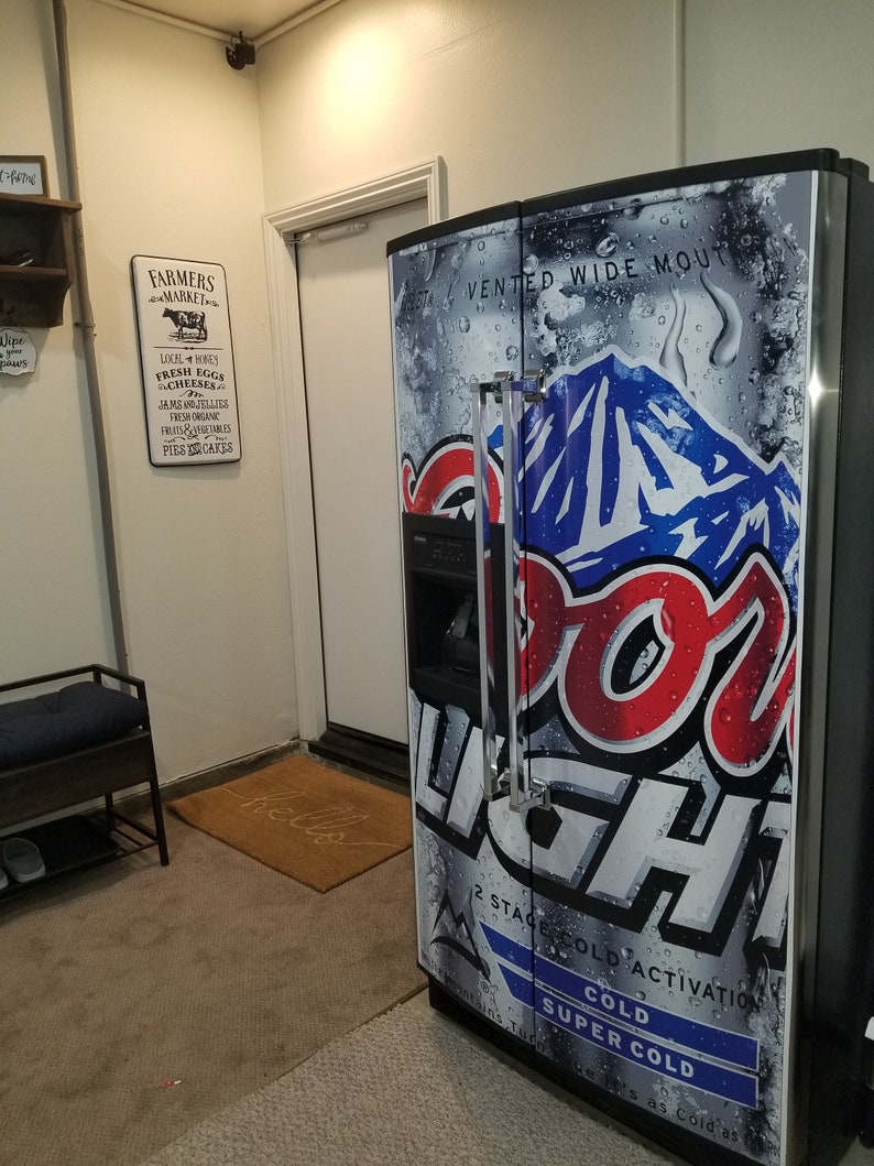 May include: A stainless steel refrigerator with a Coors Light can design on the door. The refrigerator has a water and ice dispenser and a vented wide mouth.