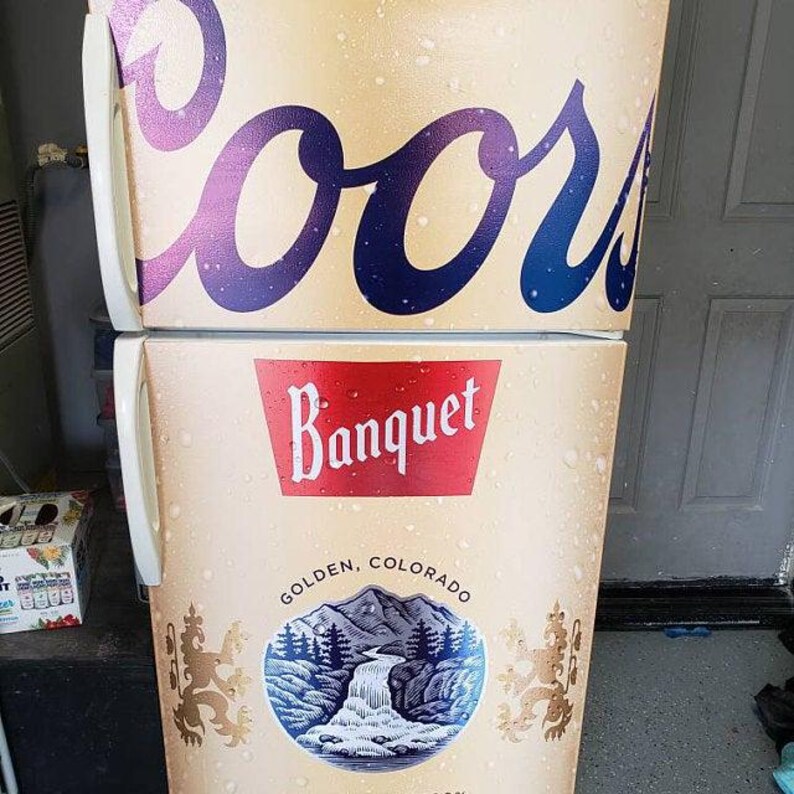 Puede incluir: Un refrigerador de dos puertas con tem&aacute;tica de cerveza Coors Banquet. El exterior es de color tostado con un patr&oacute;n de condensaci&oacute;n, mostrando el gran logotipo azul de Coors, una banda roja de Banquet y un gr&aacute;fico de monta&ntilde;as, cascada y leones.