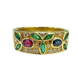 May include: A gold ring with a floral design. The ring features green, red, and blue gemstones, along with small clear stones. The gemstones are set in a pattern of leaves and flowers. The ring is set against a white background.