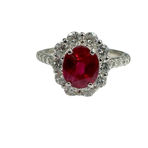 May include: A silver ring with a large oval ruby surrounded by a halo of smaller diamonds. The band is also set with diamonds.