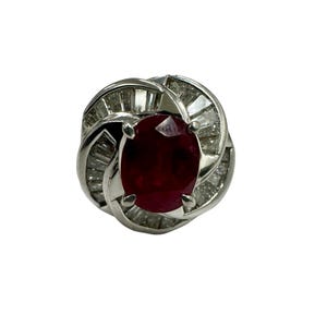 May include: A silver ring featuring a large red ruby gemstone surrounded by smaller diamonds.