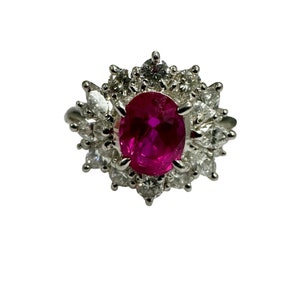 May include: A ring with a large oval ruby surrounded by a halo of smaller diamonds.