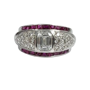 May include: A silver ring with a large, clear, emerald-cut diamond surrounded by smaller diamonds. The ring is accented with two rows of ruby stones.