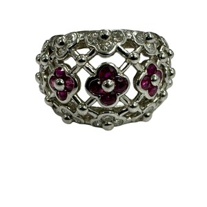 May include: A silver ring with a delicate design featuring three ruby flowers surrounded by smaller diamond flowers.