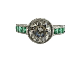 May include: A silver ring with a large round diamond and emerald green stones set in the band.