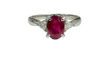 May include: A platinum ring featuring a red ruby gemstone with two smaller diamonds on either side.