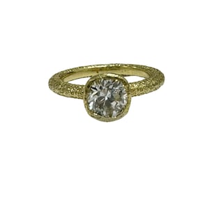 Puede incluir: Un anillo de oro con una banda texturizada y un diamante redondo y transparente.