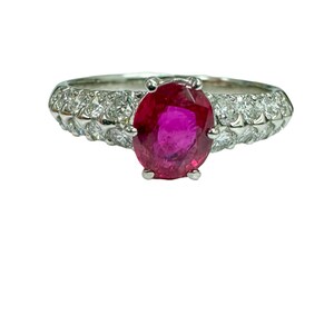 May include: A silver ring with a large oval ruby gemstone surrounded by smaller diamonds.