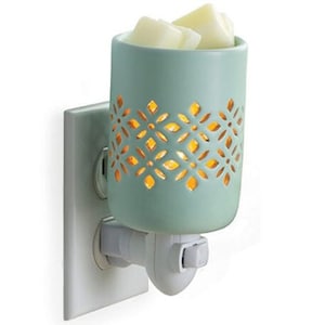 May include: A light green ceramic electric wax warmer with a decorative cut-out design. The warmer is plugged into a standard electrical outlet and has a white switch. The warmer is filled with wax melts.