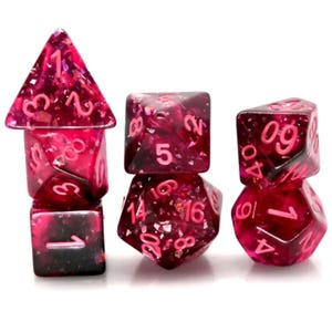 Op de afbeelding: Een set van zeven polyhedrale dobbelstenen in roze en rode tinten. De dobbelstenen zijn transparant met glitterinsluitsels en roze nummering. De set bevat een d4, d6, d8, d10, d12, d20 en een percentieldobbelsteen.