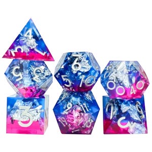 May include: A set of seven polyhedral dice for tabletop games. The dice are made of clear resin with blue, pink, and silver foil inclusions. Each die has white numbers.
