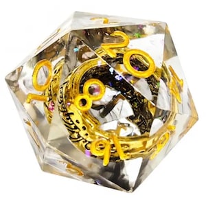Puede incluir: Un dado D20 transparente y multifacético con números dorados y un diseño interior dorado detallado. El dado está lleno de pequeñas piezas de purpurina de colores, creando un efecto brillante. Un accesorio de juego único.