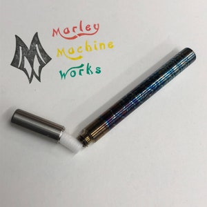 May include: A blue and silver metal pen with a white cotton swab inside. The pen is open and the swab is visible. The pen is labeled "Marley Machine Works" in red, yellow, and green.