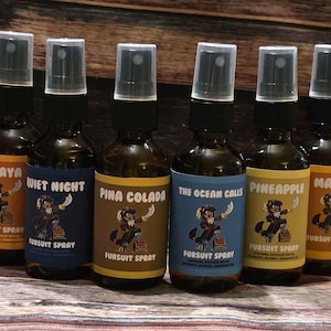 May include: Six brown glass spray bottles with black spray nozzles. Each bottle has a label with a different flavor name: Papaya, Quiet Night, Pina Colada, The Ocean Calls, Pineapple, and Mango. The labels feature a cartoon character.
