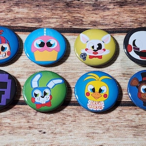 May include: A collection of eight round pinback buttons featuring colorful cartoon character designs. The buttons are blue, green, yellow, purple, and black, with various character faces and the text "LET'S PARTY!" on one.