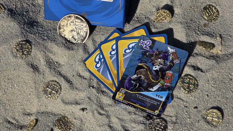 Pode incluir: Um jogo de cartas com uma caixa azul, cartas e moedas de ouro na areia. As cartas apresentam uma personagem de desenho animado com cabelo roxo e o texto "YCH". Uma moeda de ouro com um desenho de lobo tamb&eacute;m est&aacute; presente.