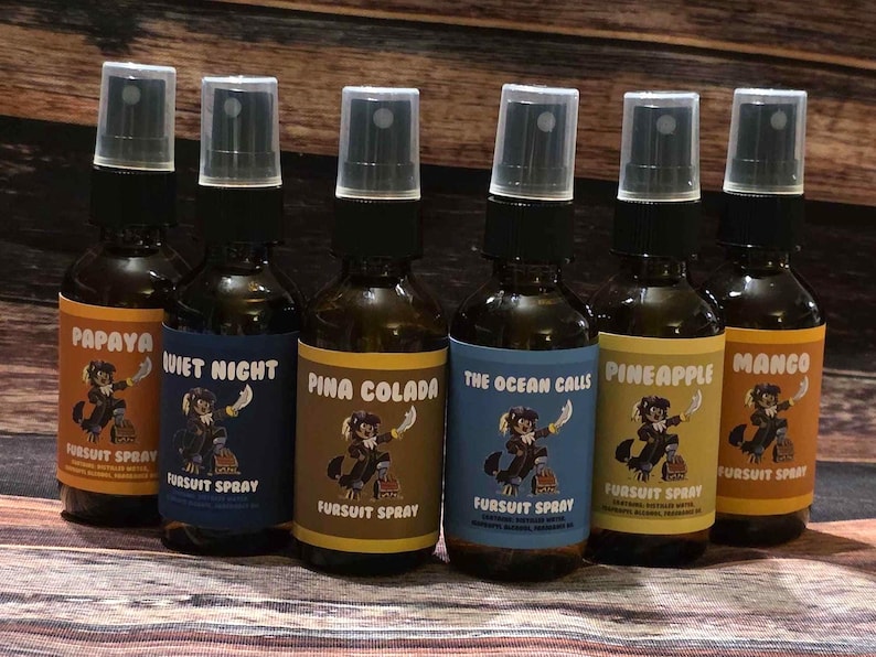 May include: Six brown glass spray bottles with black spray nozzles. Each bottle has a label with a different flavor name: Papaya, Quiet Night, Pina Colada, The Ocean Calls, Pineapple, and Mango. The labels feature a cartoon character.