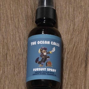 May include: A dark brown spray bottle with a black cap. The label reads "THE OCEAN CALLS FURSUIT SPRAY" with a cartoon character illustration. The bottle contains distilled water, isopropyl alcohol, and fragrance oil.