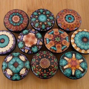 May include: A collection of ten circular cabinet knobs featuring diverse, intricate, and symmetrical patterns in vibrant shades of teal, orange, brown, and cream. Each knob displays a unique, detailed design with repeating geometric motifs.