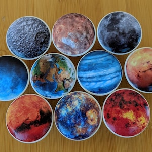 May include: Set of ten round ceramic knobs featuring images of planets in our solar system. The knobs are white with a glossy finish. The planets include Earth, Mars, Jupiter, Saturn, Uranus, Neptune, Mercury, Venus, and Pluto.