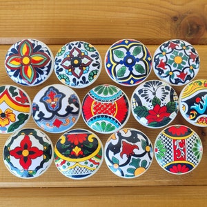 May include: A collection of fifteen ceramic cabinet knobs with colorful, hand-painted designs. Each knob features a unique pattern with vibrant hues of red, blue, yellow, and green. The knobs are round and have a diameter of approximately 1.5 inches.