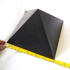 May include: A black pyramid-shaped object is being measured with a yellow tape measure. The tape measure reads 6 inches.