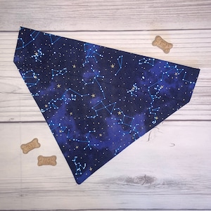 May include: A blue and gold dog bandana with a constellation pattern. The bandana is made of fabric and has a triangular shape.
