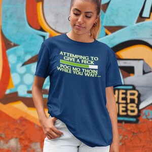 A young woman wearing a blue t-shirt with a humorous text printed on it, standing in front of a colorful graffiti wall.