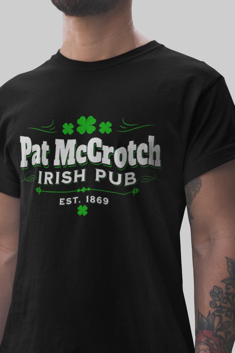 A Funny St. Patrick's t-shirt in black color, with white text and green shamrocks printed on it spelling the words 'Pat McCrotch'