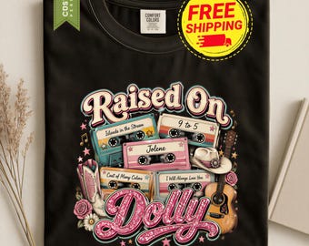 May include: A black t-shirt featuring a graphic print with the text "Raised On Dolly" in pink glitter-style lettering. The design includes four cassette tapes labeled "Islands in the Stream," "9 to 5," "Jolene," and "Coat of Many Colors."