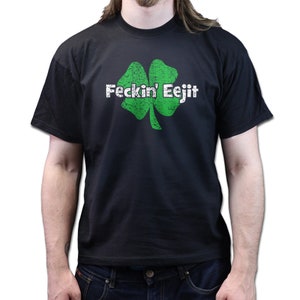 May include: Black t-shirt featuring a distressed green shamrock graphic with the text "Feckin' Eejit" in white. The shirt is a crew neck style and is made of a soft material.