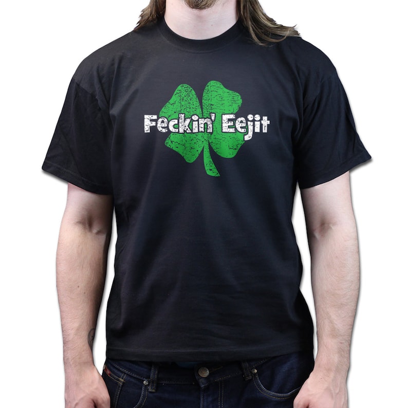 May include: Black t-shirt featuring a distressed green shamrock graphic with the text "Feckin' Eejit" in white. The shirt is a crew neck style and is made of a soft material.