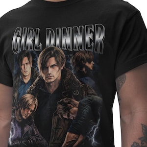 Könnte beinhalten: Schwarzes T-Shirt mit einem silbernen, umrandeten Schriftzug "GIRL DINNER". Das Design zeigt mehrere Bilder eines Mannes in verschiedenen Posen, mit Blitzeffekten im Hintergrund.