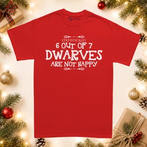 May include: A bright red short-sleeved t-shirt featuring white text that reads: STATISTICALLY 6 OUT OF 7 DWARVES ARE NOT HAPPY. The design includes decorative flourishes above and below the text, centred on the front of the garment.