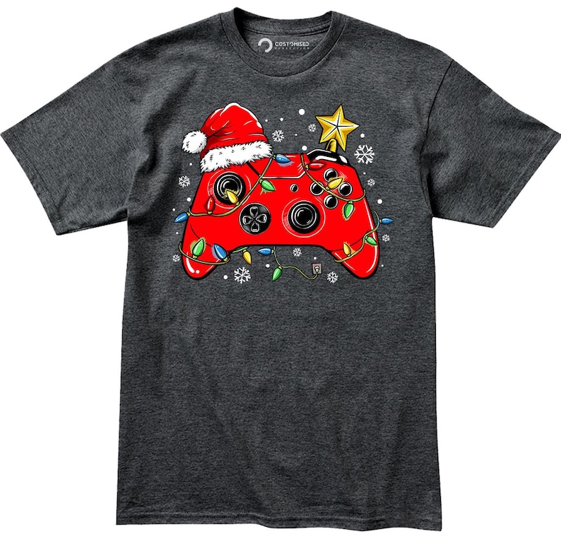 K&ouml;nnte beinhalten: Ein dunkelgraues T-Shirt mit einem roten Videospiel-Controller, der mit Weihnachtslichtern und einer Weihnachtsm&uuml;tze verziert ist. Der Controller ist mit einer gr&uuml;nen, roten und gelben Lichterkette umwickelt.