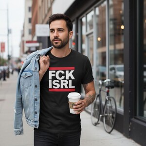 A man wearing a black t-shirt with the text "FCK ISRL" is walking down a city street while holding a coffee cup.