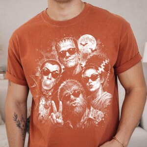 a man wearing a red t-shirt with a graphic design of a group of people, including a woman with a skull and crossbones, a man with a mustache, and a woman with a bride-to-be face.