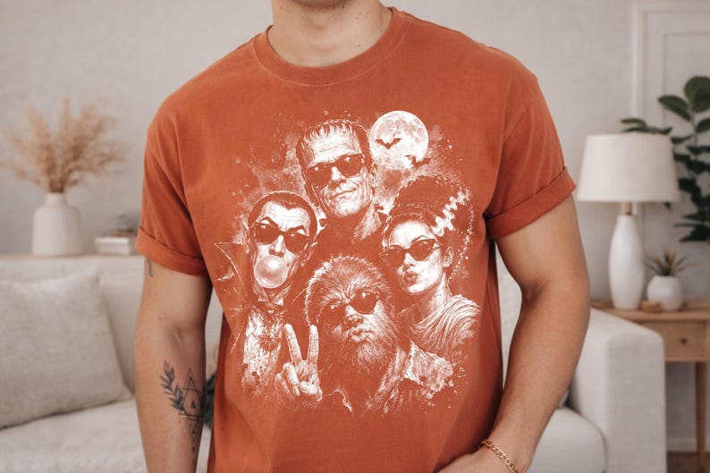 a man wearing a red t-shirt with a graphic design of a group of people, including a woman with a skull and crossbones, a man with a mustache, and a woman with a bride-to-be face.