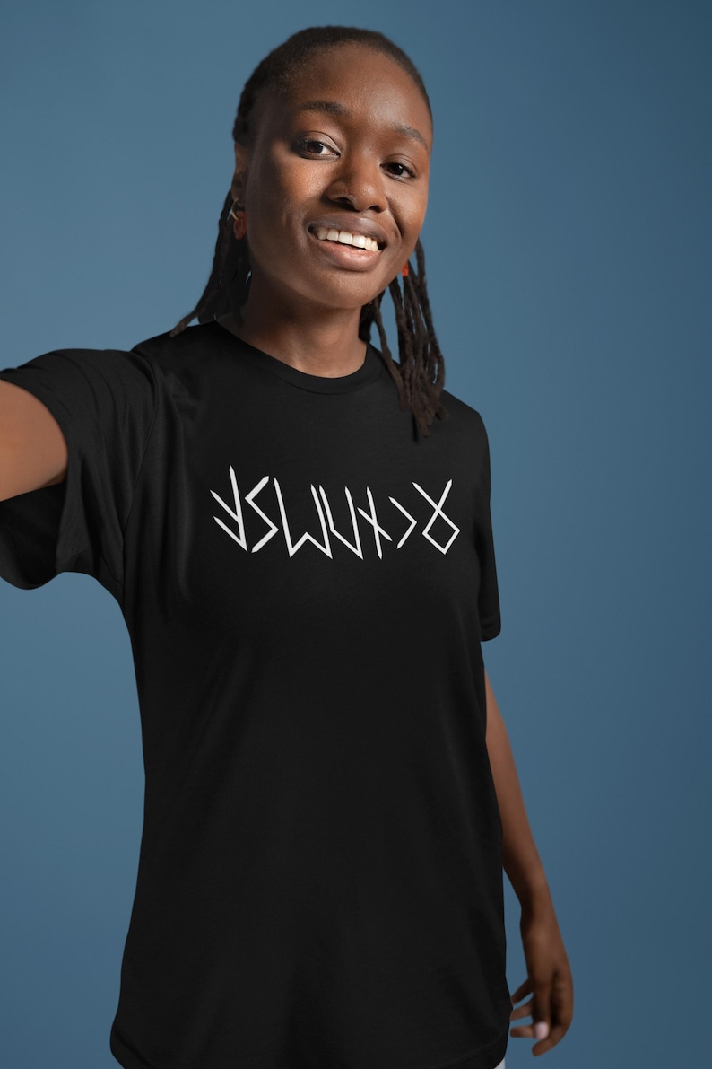 A smiling young woman wearing a black t-shirt with white text on it.