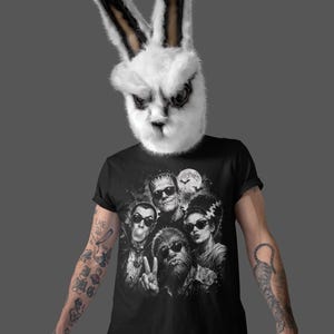 A person wearing a bunny mask and a black t-shirt with a graphic design of a group of people.