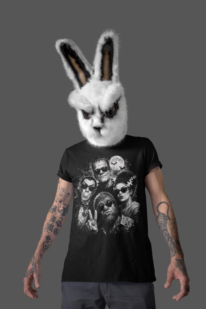 A person wearing a bunny mask and a black t-shirt with a graphic design of a group of people.