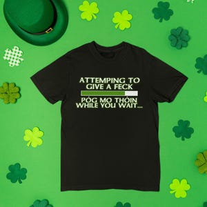 a black t-shirt with a humorous text printed on it, surrounded by shamrocks and a green hat, all set against a green background.