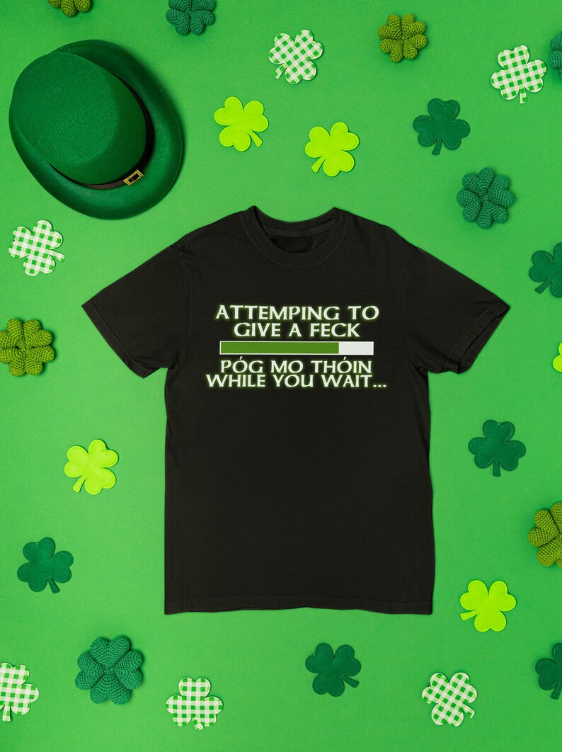 a black t-shirt with a humorous text printed on it, surrounded by shamrocks and a green hat, all set against a green background.